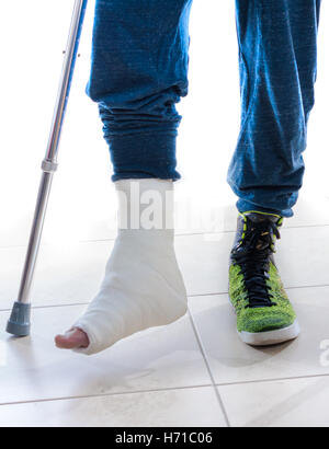 Young man with a broken ankle and a white cast on his leg following a basketball accident, walking on crutches and a high-top ba Stock Photo