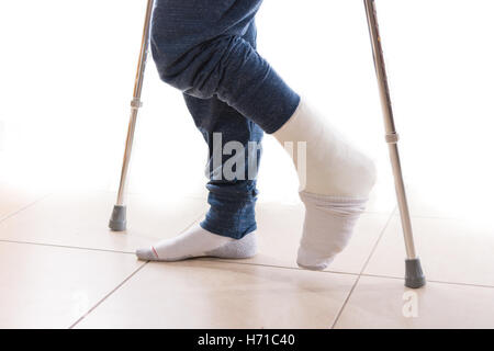 Young man with a broken ankle and a white leg cast with a sock to help keeping his toes warm, walking on crutches (isolated on w Stock Photo