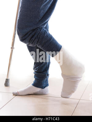 Young man with a broken ankle and a white leg cast with a sock to help keeping his toes warm, walking on crutches (isolated on w Stock Photo