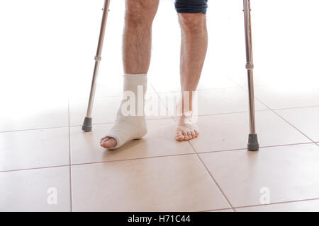 Young man with a broken ankle and a white cast on his leg, walking on crutches (isolated on white) Stock Photo