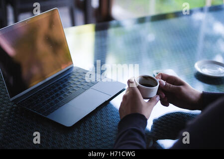 Fresh coffee for great ideas. Top view man working on laptop and holding cup of coffe while sitting at cafe Stock Photo