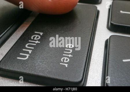 computer enter key with finger pressing button Stock Photo