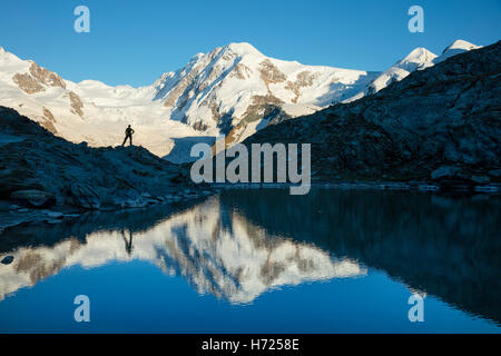 Hiker and Lyskamm reflected in the Riffelsee, Zermatt, Pennine Alps, Valais, Switzerland.
