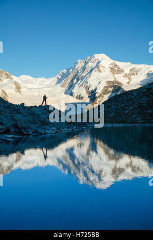 Hiker and Lyskamm reflected in the Riffelsee, Zermatt, Pennine Alps, Valais, Switzerland. Stock Photo