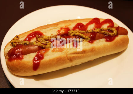 A freshly grilled hotdog on a bun with a stream of mustard and ketchup on a plate Stock Photo