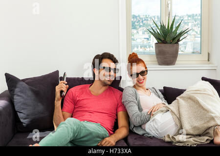 young couple sitting with 3d glasses on the sofa and looks remote Stock Photo