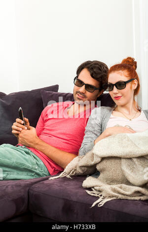young couple sitting with 3d glasses on the sofa and looks remote Stock Photo