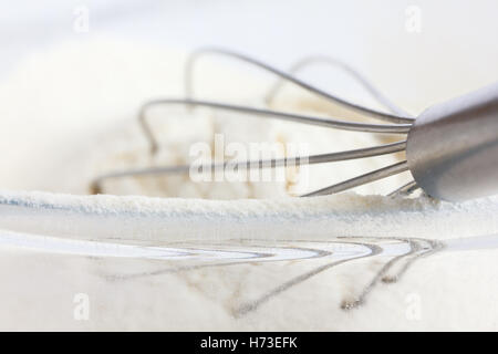 Whisk lying in white wheat flour in a glass dish. Flour on rim of bowl. Stock Photo