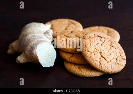 Fresh cut root ginger next to a pile of ginger biscuits isolated on dark wood. Stock Photo