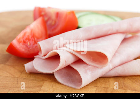 Processed ham randomly arranged on chopping board. Tomato and cucumber. Stock Photo