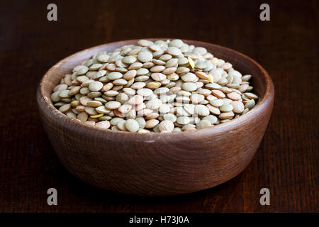 Rustic bowl of green uncooked lentils isolated on dark wood in perspective. Stock Photo