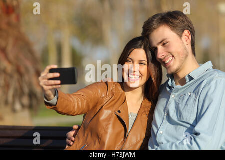 Couple taking selfie photo sitting in a bench Stock Photo