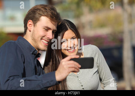 Happy couple watching media in a smart phone outdoors Stock Photo