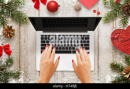 Woman work on laptop. Christmas scene with decorations, tree and gift. Blank screen for mockup. Top view of table. Stock Photo
