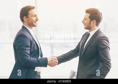 Two handsome colleagues shaking hands in an office. Stock Photo