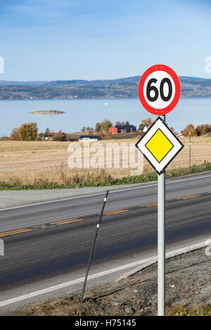 Vertical photo of Main road yellow roadsign with speed limit road sign mounted on one metal pole near rural Norwegian road Stock Photo