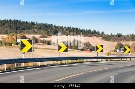 Dangerous turn. Yellow arrows in black square roadsigns along turning highway, rural Norwegian road Stock Photo