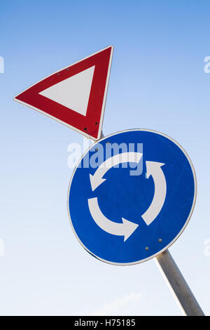 Triangle Give way and round Traffic roundabout road signs on one metal pole over blue sky Stock Photo