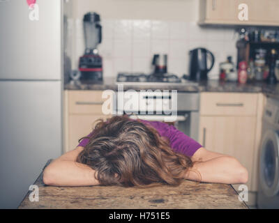 A young woman is resting her head on a table in a kitchen Stock Photo