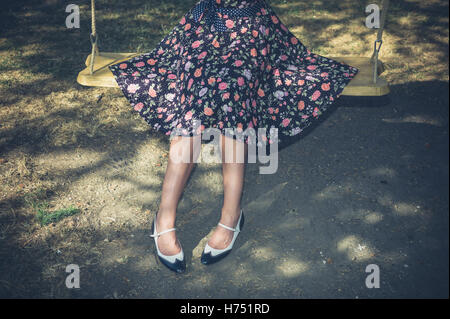 A young woman wearing a dress is sitting on a swing outside on a summer day Stock Photo