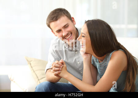 Happy couple or marriage looking each other laughing and holding hands sitting on a sofa at home Stock Photo