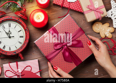Female hands holding christmas gift above wooden table. Top view. Xmas gift wrapping Stock Photo