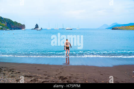 The black sand beach with yachts in small haven and young man, going to swim, in Porto di Ponente Stock Photo