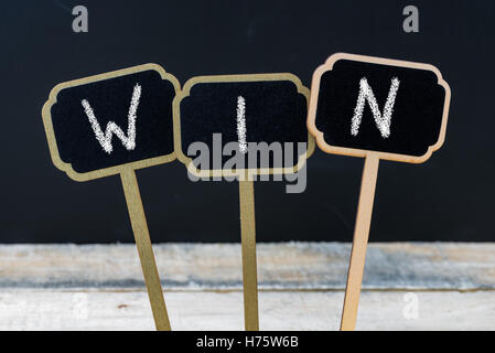 Word WIN written with chalk on wooden mini blackboard labels, defocused chalkboard and wood table in background Stock Photo