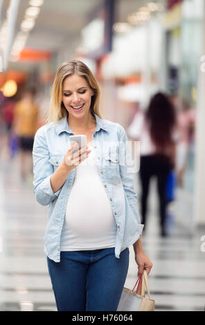 Pregnant woman with smartphone in shopping center, texting Stock Photo