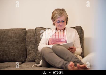 Senior woman with tablet sitting on couch in living room Stock Photo