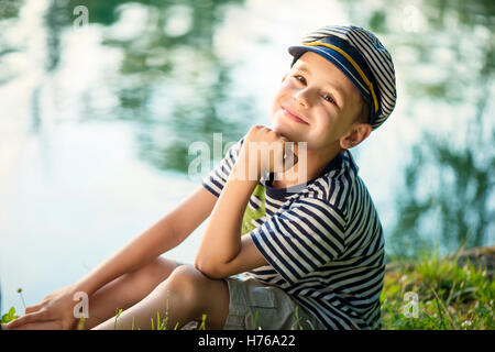 Portrait of a boy sitting by a river wearing a sailor outfit Stock Photo