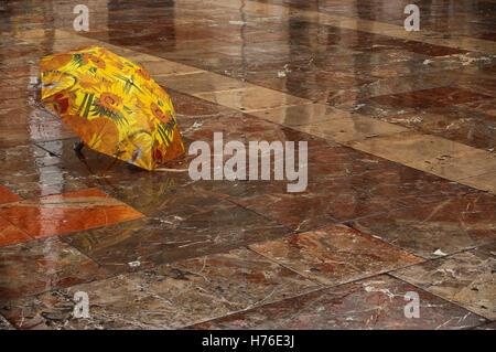 Open umbrella with floral pattern, on the rain-wet marble tile floor and with reflections of the buildings. Valencia Spain Stock Photo