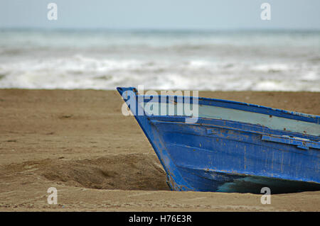 Boat half buried in the sand on the beach with ocean waves out of focus in the background. Sad light of rainy day. Copy space Stock Photo