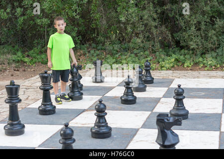 Boy playing a game of giant outdoor chess with big pieces in a green outdoor park Stock Photo