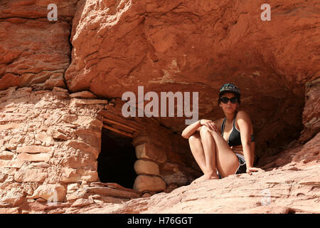 An athletic young woman sits next to a small cliff dwelling on the Green River, in Canyonlands National Park Stock Photo