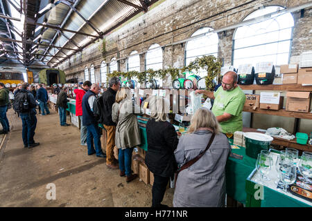 CAMRA beer festival in old locomotive shed at Tunbridge Wells, UK. People selecting beers from various casks, beer barrels, behind a long counter. Stock Photo