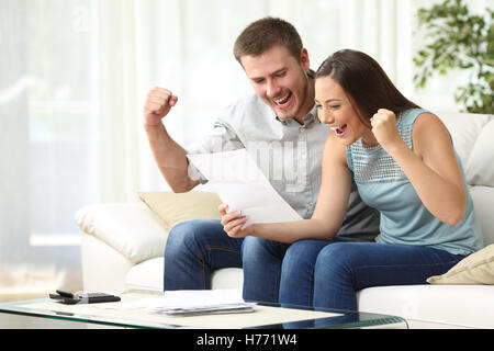 Excited couple reading a letter together sitting on a sofa in the living room at home Stock Photo