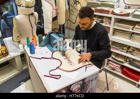 Man using a stitching machine to stitch the name "Christoph" in script typeface on a baby bib. Stock Photo