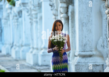 Young woman holding flowers outside temple, Mandalay, Myanmar Stock Photo