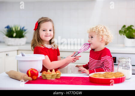 Little boy and girl, brother and sister baking delicious apple pie in white kitchen. Kids looking at fruit cake in the oven. Stock Photo