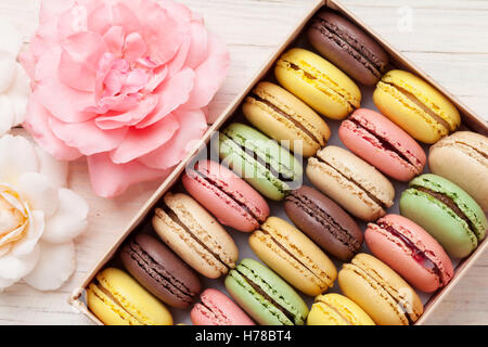 Colorful macaroons in a gift box on wooden table. Sweet macarons and flowers. Top view Stock Photo