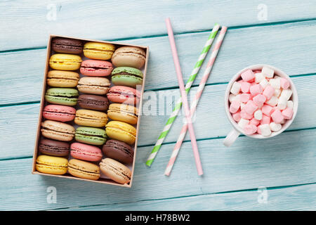 Colorful macaroons and coffee cup with marshmallow on wooden table. Sweet macarons in gift box. Stock Photo