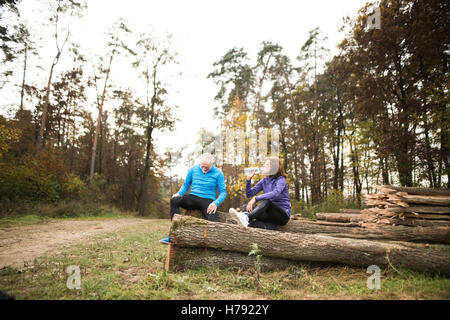 Senior runners sitting on wooden logs, resting, drinking water. Stock Photo