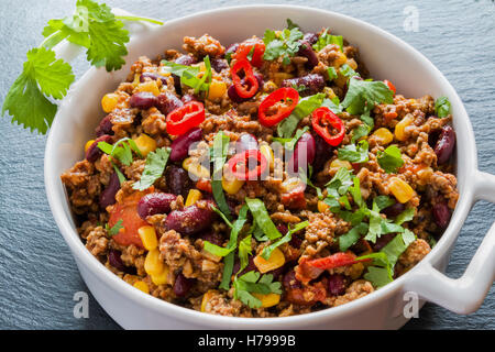 Chili con carne in a white casserole on black stone background. Cooked with ground beef, tomatoes, peppers, beans, corn, garlic, Stock Photo