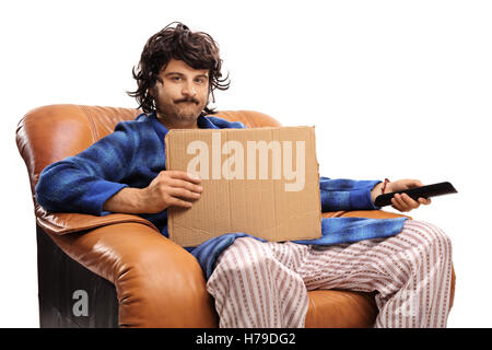 Disappointed retro guy seated in an armchair holding a remote control and a blank cardboard sign isolated on white background Stock Photo