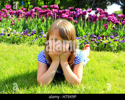 little fashionable school girl lays on the grass and besides tulips Stock Photo