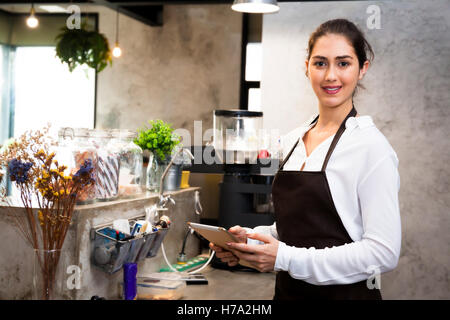 Beautiful Caucasian female barista using tablet and smiling inside coffee shop Stock Photo