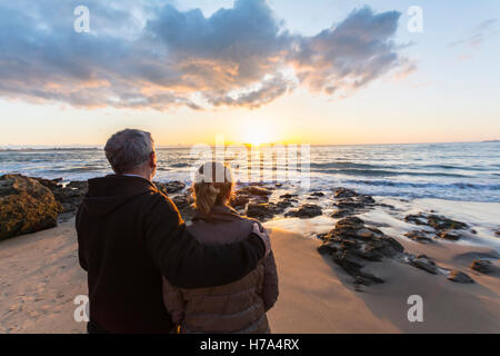 Couple in love watching a sunset on the beach, moment of reflection Stock Photo