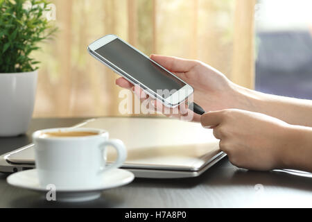 Girl hand connecting charger to smart phone in a table at home with a window in the background Stock Photo