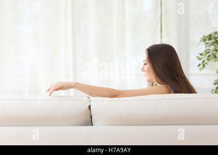 Sad woman sitting on a couch missing her lost husband touching the empty seat at home Stock Photo